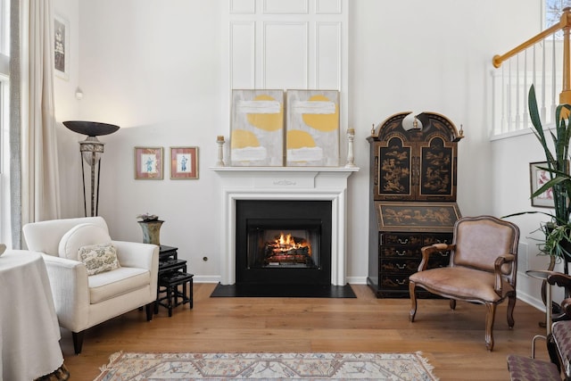 living area featuring a fireplace with flush hearth, wood finished floors, and baseboards