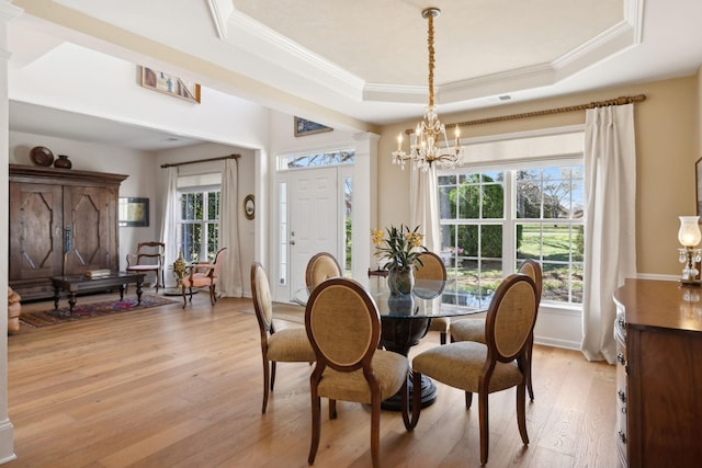 dining area with ornate columns, a tray ceiling, light wood-style flooring, crown molding, and a chandelier