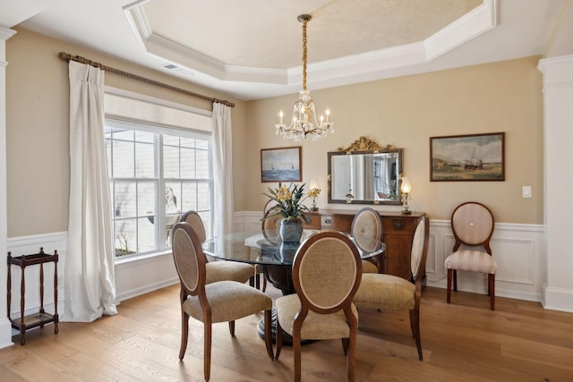 dining area with a raised ceiling, a notable chandelier, wainscoting, and light wood finished floors