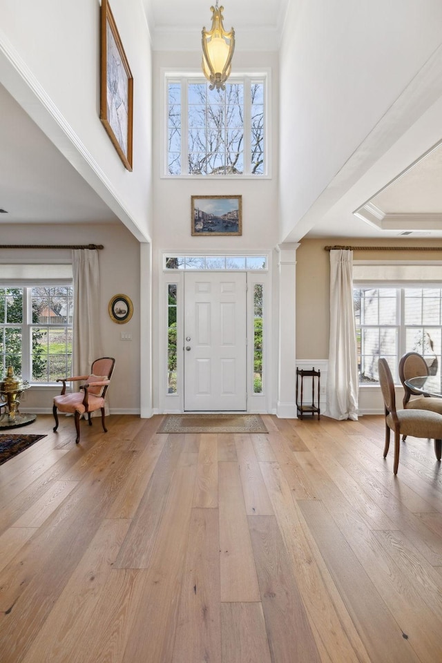 foyer entrance featuring baseboards, plenty of natural light, crown molding, and light wood finished floors