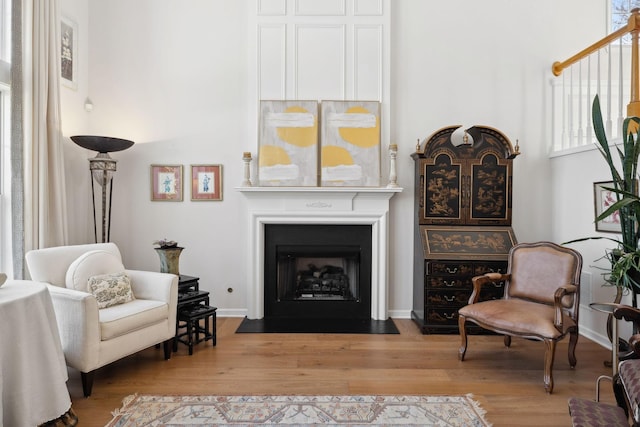 sitting room featuring a fireplace with flush hearth, baseboards, and wood finished floors