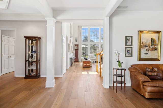 foyer entrance featuring beam ceiling, light wood-style flooring, baseboards, and decorative columns