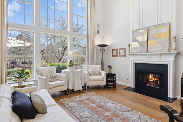 living area with a glass covered fireplace, a high ceiling, baseboards, and wood finished floors