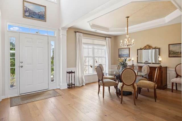 entryway featuring a wainscoted wall, light wood-style flooring, crown molding, a raised ceiling, and a chandelier