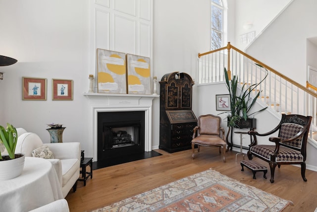 sitting room featuring stairway, a fireplace with flush hearth, light wood-style floors, and a high ceiling