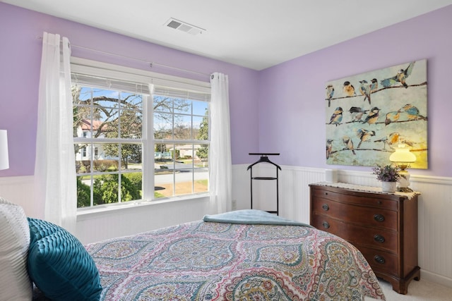 bedroom with visible vents, wainscoting, light colored carpet, and multiple windows