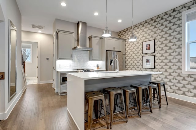 kitchen with visible vents, wall chimney range hood, light wood-type flooring, gray cabinets, and stainless steel refrigerator with ice dispenser