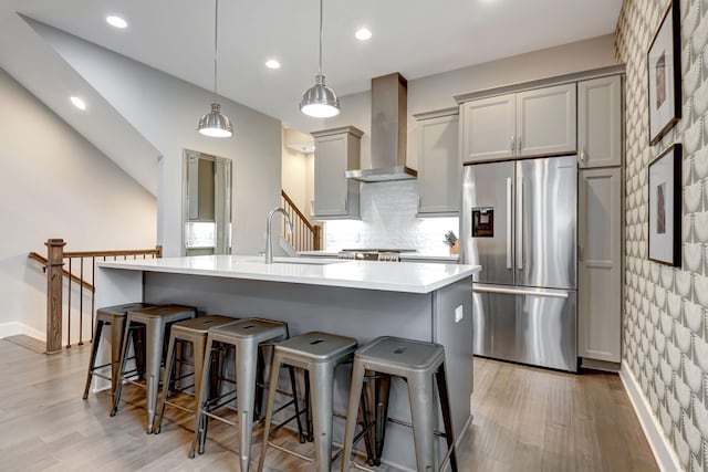 kitchen with a sink, gray cabinetry, light wood-style floors, wall chimney range hood, and stainless steel fridge