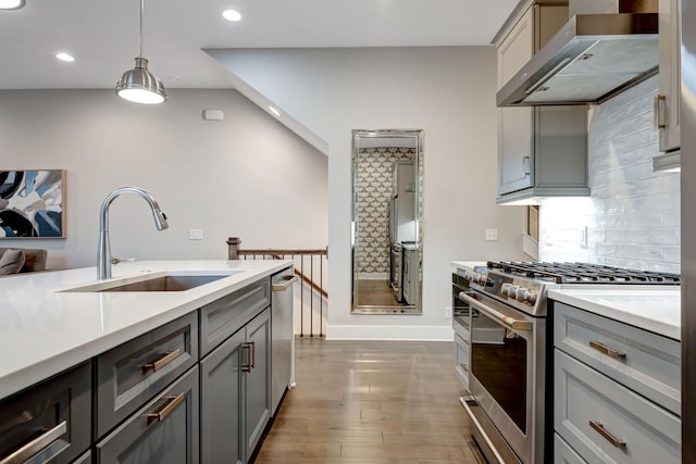 kitchen featuring range hood, gray cabinetry, a sink, light countertops, and appliances with stainless steel finishes