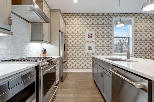 kitchen featuring gray cabinets, a sink, wall chimney range hood, stainless steel appliances, and light countertops