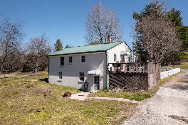 back of property featuring a wooden deck, a lawn, a chimney, and metal roof