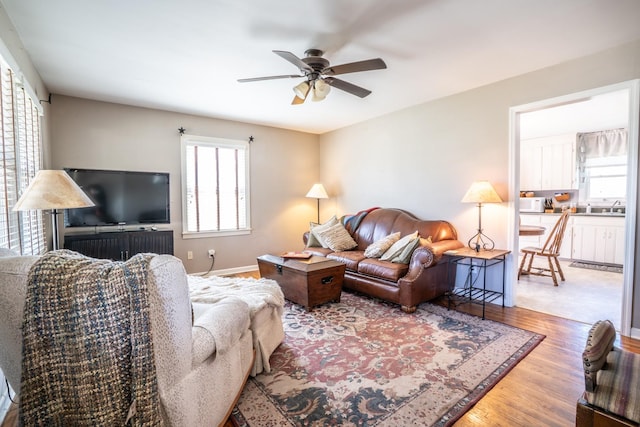 living area with baseboards, wood finished floors, and a ceiling fan