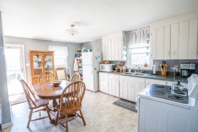 kitchen with a sink, dark countertops, white cabinetry, white appliances, and light floors