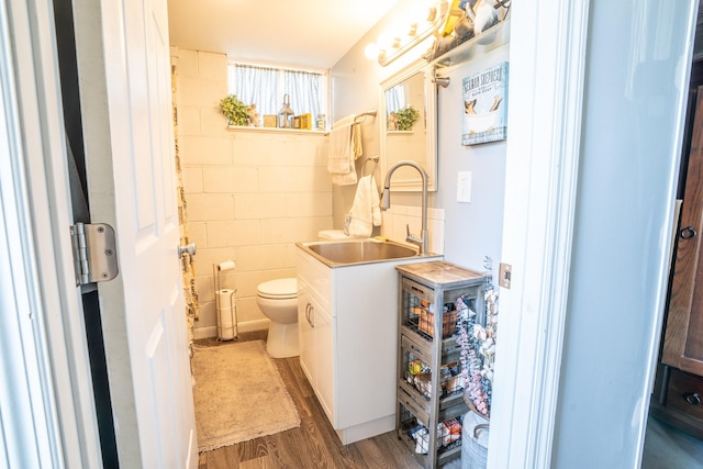 bathroom featuring concrete block wall, toilet, wood finished floors, and vanity