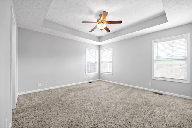 carpeted empty room featuring baseboards, visible vents, ceiling fan, a textured ceiling, and a raised ceiling