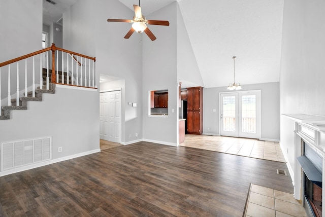 unfurnished living room with visible vents, stairway, ceiling fan with notable chandelier, a fireplace, and wood finished floors