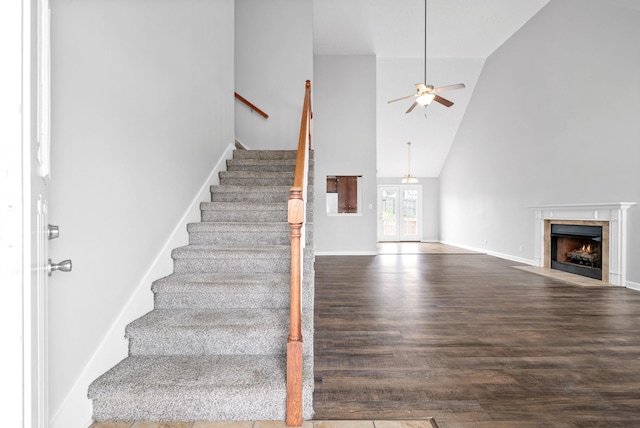 staircase with wood finished floors, baseboards, high vaulted ceiling, a tile fireplace, and ceiling fan