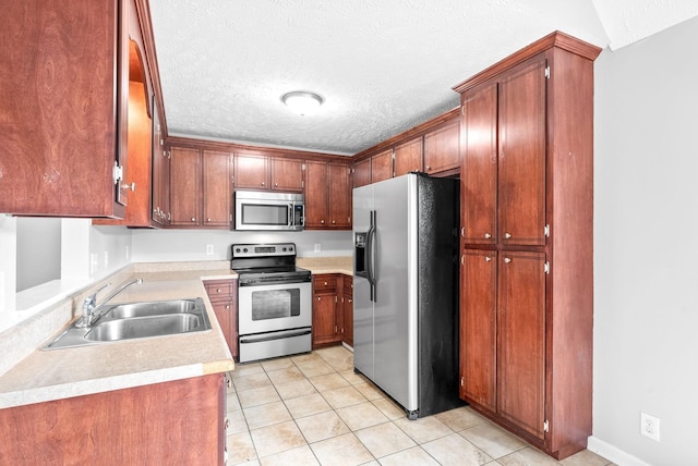 kitchen with light countertops, appliances with stainless steel finishes, light tile patterned flooring, a textured ceiling, and a sink