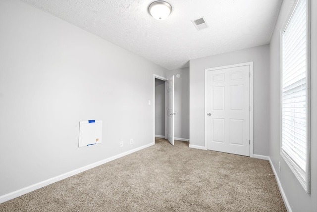 unfurnished bedroom featuring carpet flooring, visible vents, a textured ceiling, and baseboards