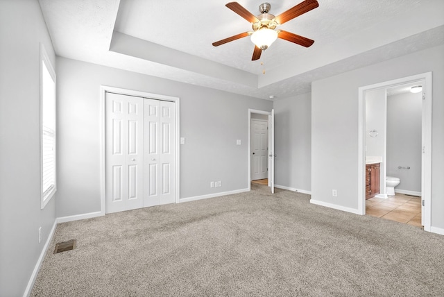 unfurnished bedroom with baseboards, visible vents, a tray ceiling, a textured ceiling, and light carpet