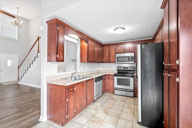 kitchen featuring a sink, a textured ceiling, stainless steel appliances, an inviting chandelier, and light countertops