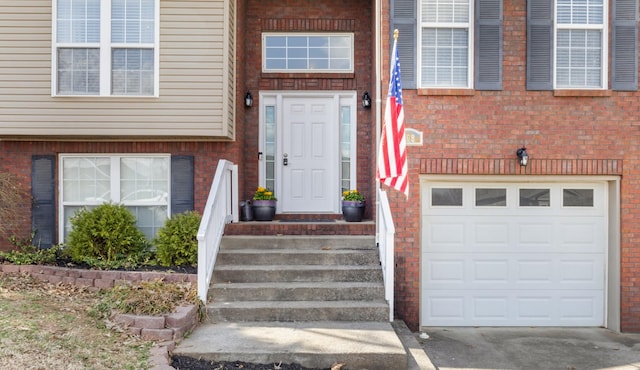 doorway to property featuring a garage, brick siding, and driveway