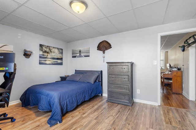 bedroom with a drop ceiling, baseboards, and wood finished floors