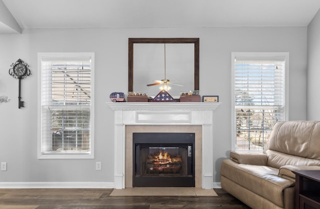 living area with a ceiling fan, a fireplace with flush hearth, wood finished floors, and baseboards