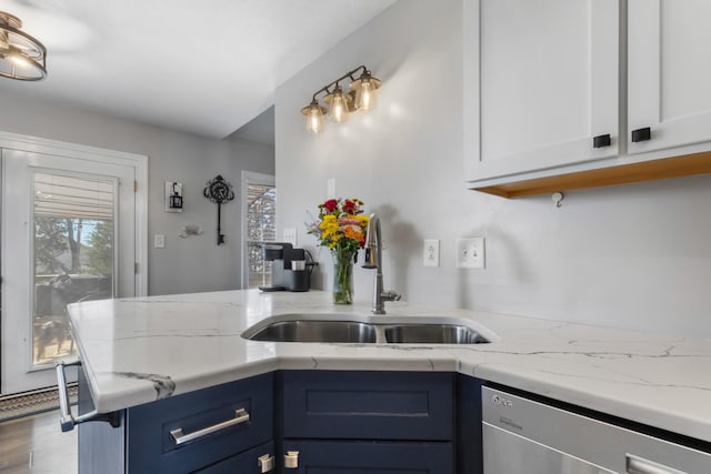 kitchen with a peninsula, stainless steel dishwasher, white cabinets, blue cabinets, and a sink