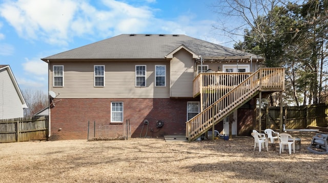 rear view of property featuring brick siding, stairway, a wooden deck, and fence