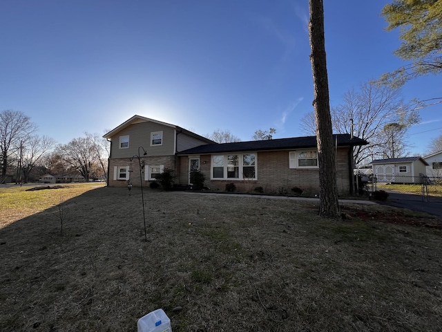 tri-level home featuring brick siding, a front lawn, and fence