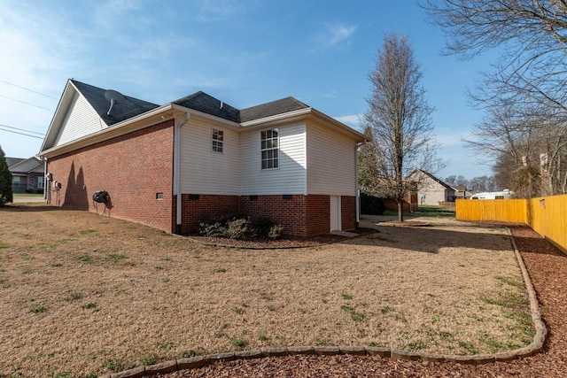 view of home's exterior featuring brick siding, a yard, and fence