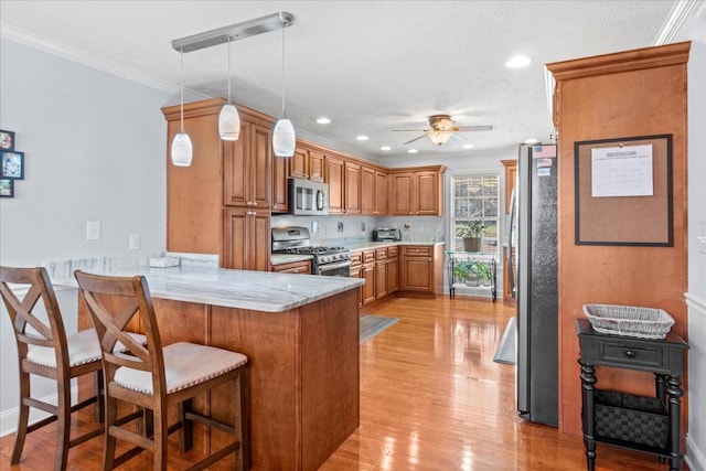 kitchen with brown cabinets, a kitchen breakfast bar, appliances with stainless steel finishes, a peninsula, and a ceiling fan