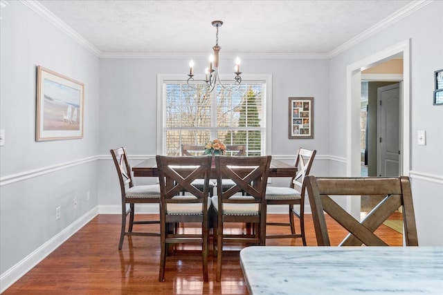 dining space featuring dark wood-type flooring, a notable chandelier, a textured ceiling, crown molding, and baseboards