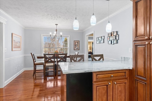 kitchen featuring decorative light fixtures, wood finished floors, a peninsula, an inviting chandelier, and brown cabinetry