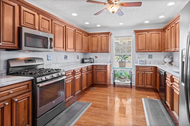 kitchen featuring light wood-style flooring, brown cabinets, appliances with stainless steel finishes, and ceiling fan