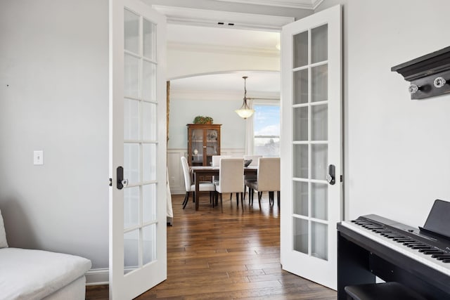 corridor featuring arched walkways, ornamental molding, dark wood-type flooring, french doors, and wainscoting