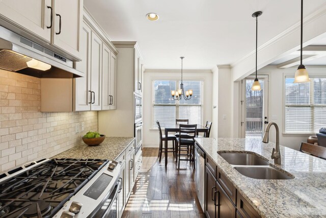 kitchen featuring under cabinet range hood, a sink, stainless steel appliances, crown molding, and a chandelier