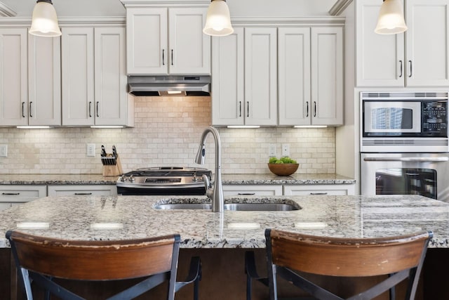 kitchen featuring under cabinet range hood, stainless steel appliances, a kitchen bar, and a sink