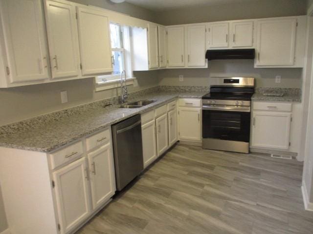 kitchen featuring light wood-type flooring, under cabinet range hood, a sink, stainless steel appliances, and white cabinets