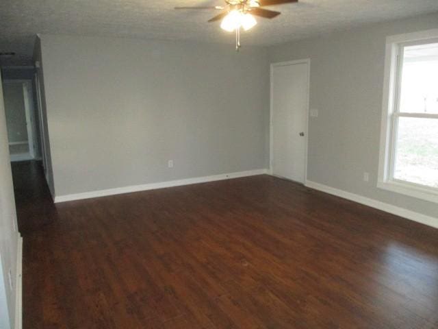 unfurnished room featuring baseboards, dark wood-type flooring, and a ceiling fan