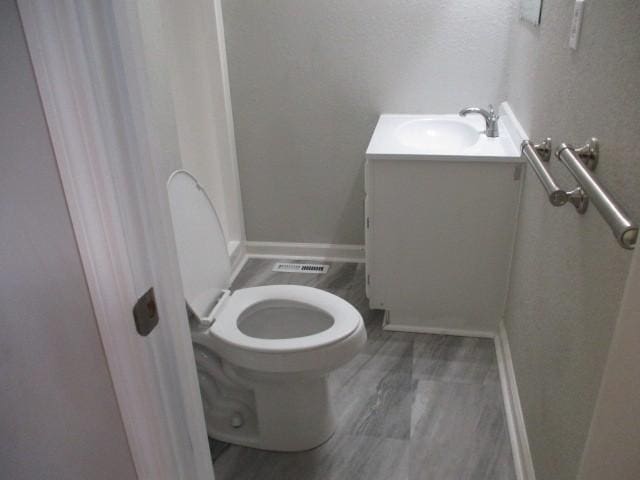 bathroom featuring visible vents, toilet, wood finished floors, baseboards, and vanity