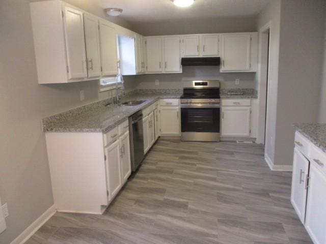 kitchen featuring under cabinet range hood, light stone counters, a sink, stainless steel appliances, and white cabinets