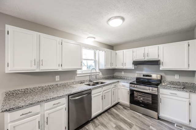 kitchen with under cabinet range hood, stainless steel appliances, a sink, a textured ceiling, and white cabinetry