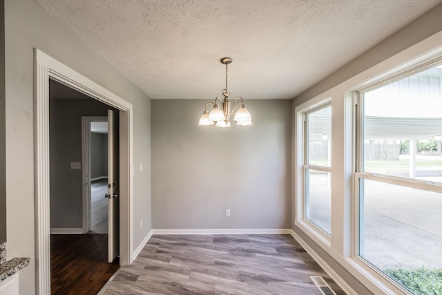 unfurnished dining area featuring a notable chandelier, wood finished floors, a wealth of natural light, and a textured ceiling