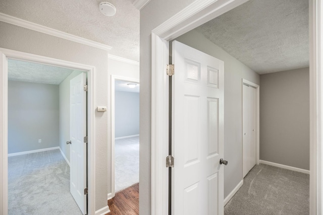 hallway with carpet floors, crown molding, a textured ceiling, and baseboards
