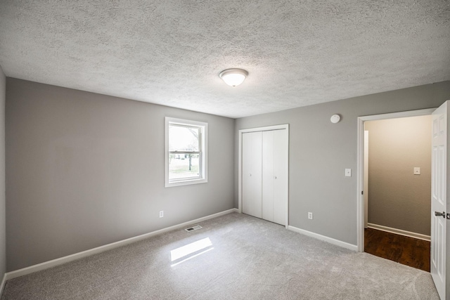 unfurnished bedroom featuring a textured ceiling, baseboards, visible vents, carpet, and a closet