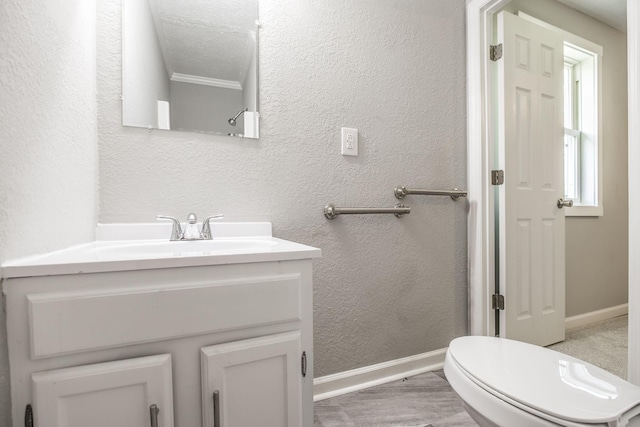 bathroom with baseboards, toilet, vanity, and a textured wall