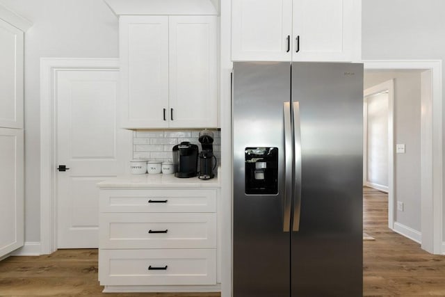 kitchen with light countertops, decorative backsplash, light wood-style flooring, stainless steel refrigerator with ice dispenser, and white cabinetry