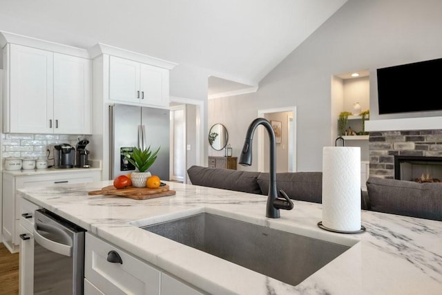 kitchen with light stone countertops, open floor plan, vaulted ceiling, stainless steel refrigerator, and a sink